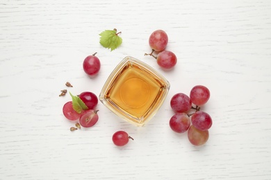 Photo of Flat lay composition with bowl of natural grape seed oil on white wooden table. Organic cosmetic
