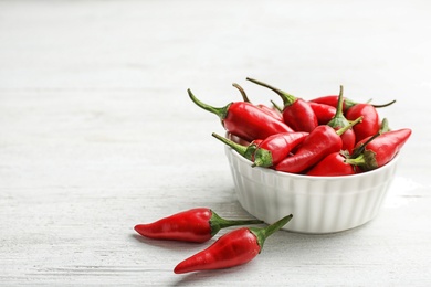 Photo of Bowl with red chili peppers on wooden table. Space for text