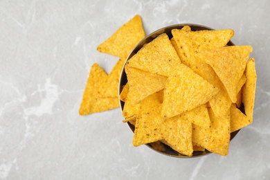 Photo of Metal bowl with tasty Mexican nachos chips on grey table, flat lay. Space for text