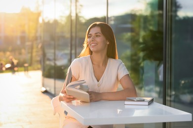 Photo of Young woman with coffee reading book in outdoor cafe on sunny day