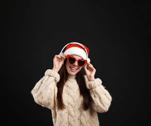 Photo of Young woman in Santa hat listening to Christmas music on black background