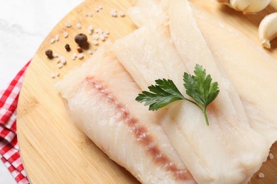 Photo of Pieces of raw cod fish, spices and parsley on table, closeup