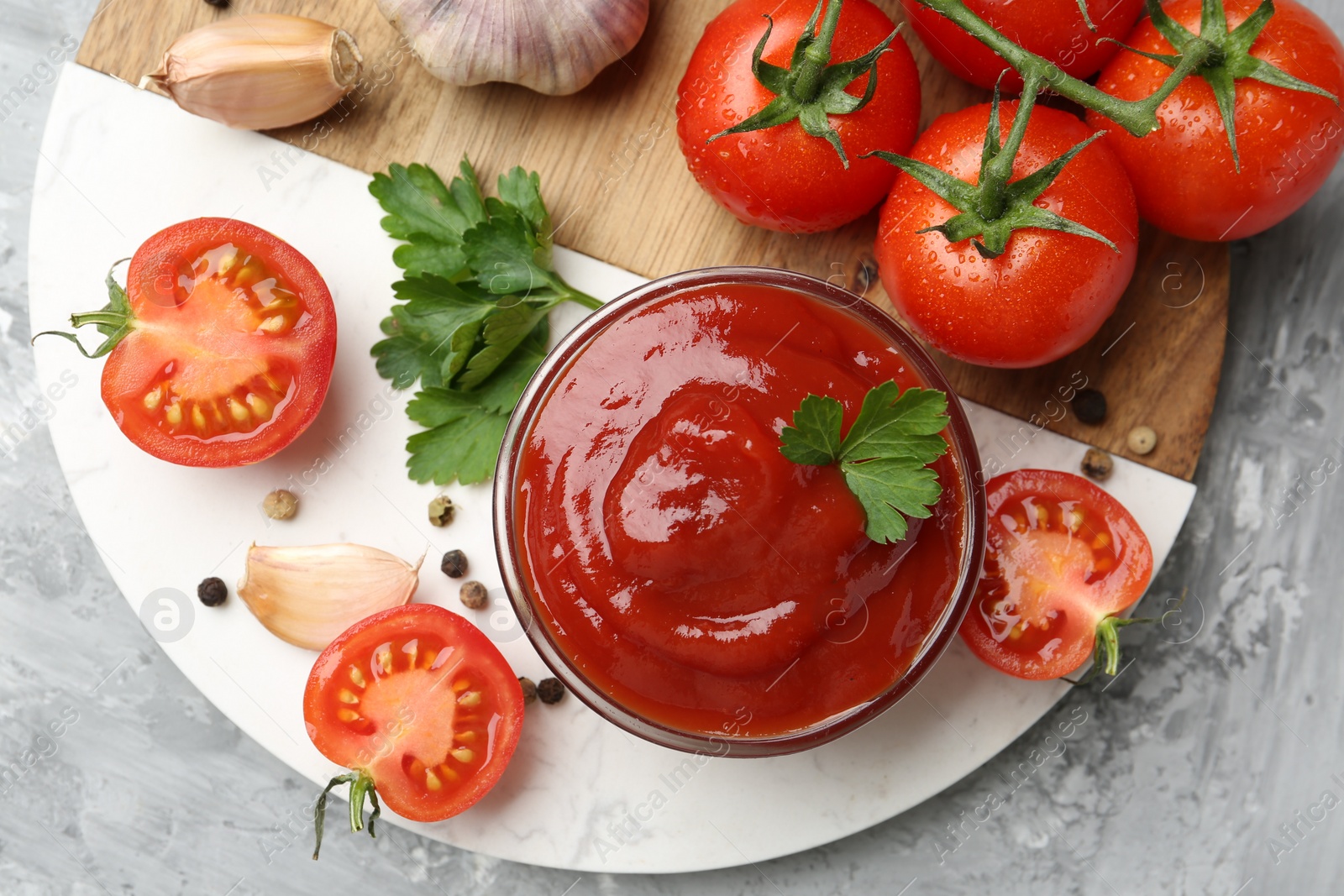 Photo of Delicious ketchup in bowl, parsley, garlic and tomatoes on grey textured table, top view