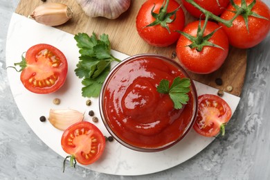 Photo of Delicious ketchup in bowl, parsley, garlic and tomatoes on grey textured table, top view
