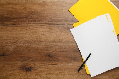 Photo of Yellow files with blank sheets of paper and pen on wooden table, flat lay. Space for text