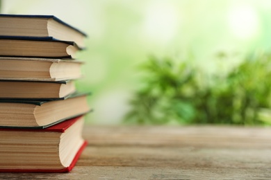 Photo of Stack of hardcover books on wooden table against blurred background. Space for text