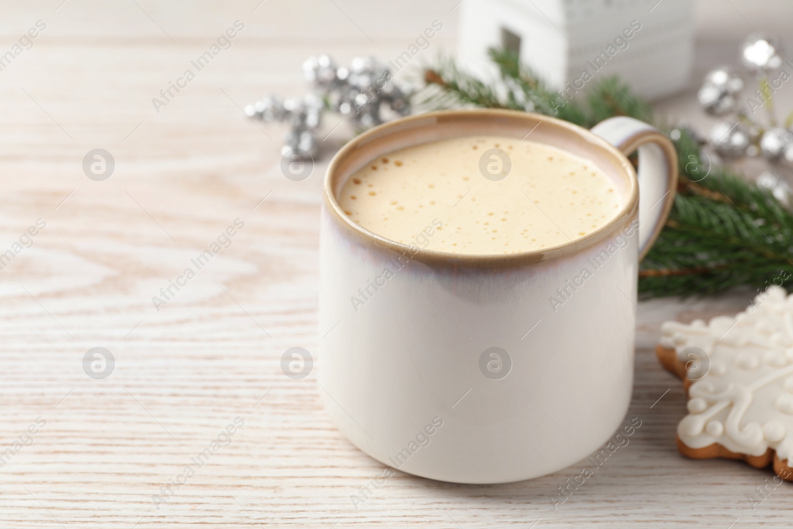 Photo of Cup of delicious eggnog and cookie on wooden table, space for text