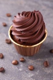 Photo of Delicious chocolate cupcake and coffee beans on grey textured table, closeup