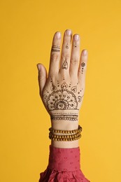 Photo of Woman with beautiful henna tattoo on hand against yellow background, closeup. Traditional mehndi