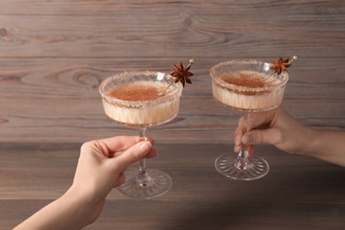 Photo of Women holding glasses with delicious eggnog at light wooden table, closeup