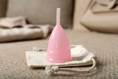 Photo of Pink menstrual cup with bag on sofa
