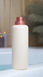 Photo of Beige bottle of bubble bath and candles on tub indoors