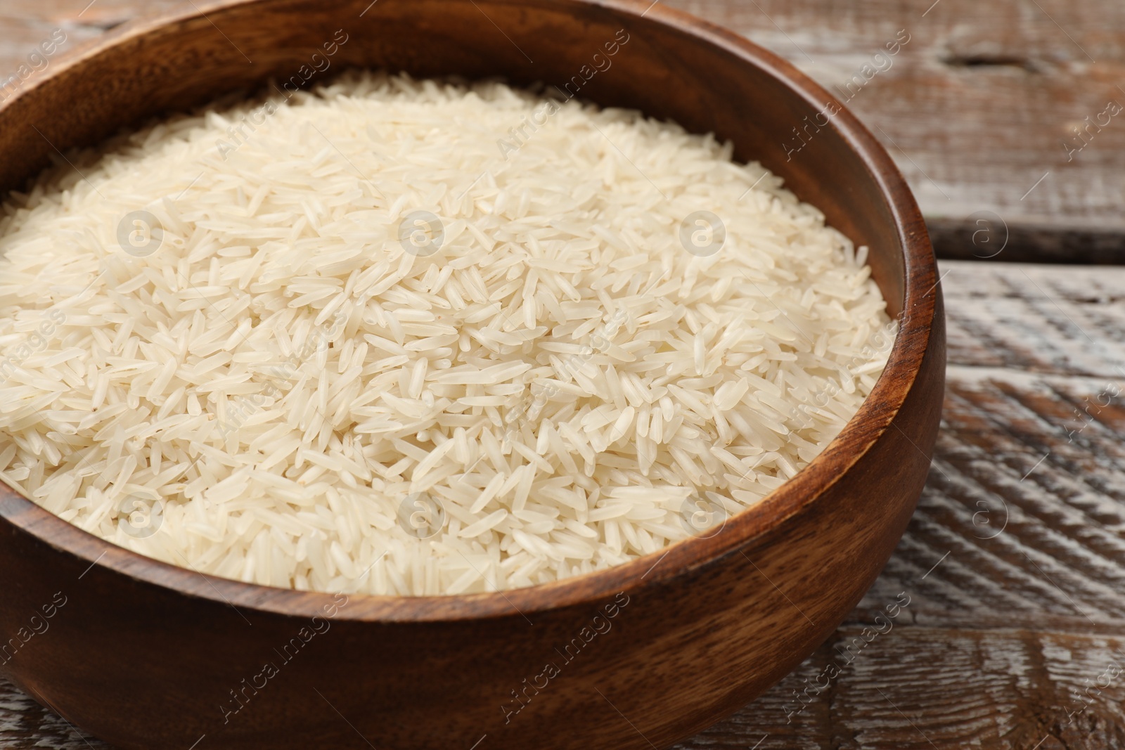 Photo of Raw basmati rice in bowl on wooden table, closeup