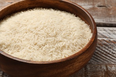 Photo of Raw basmati rice in bowl on wooden table, closeup