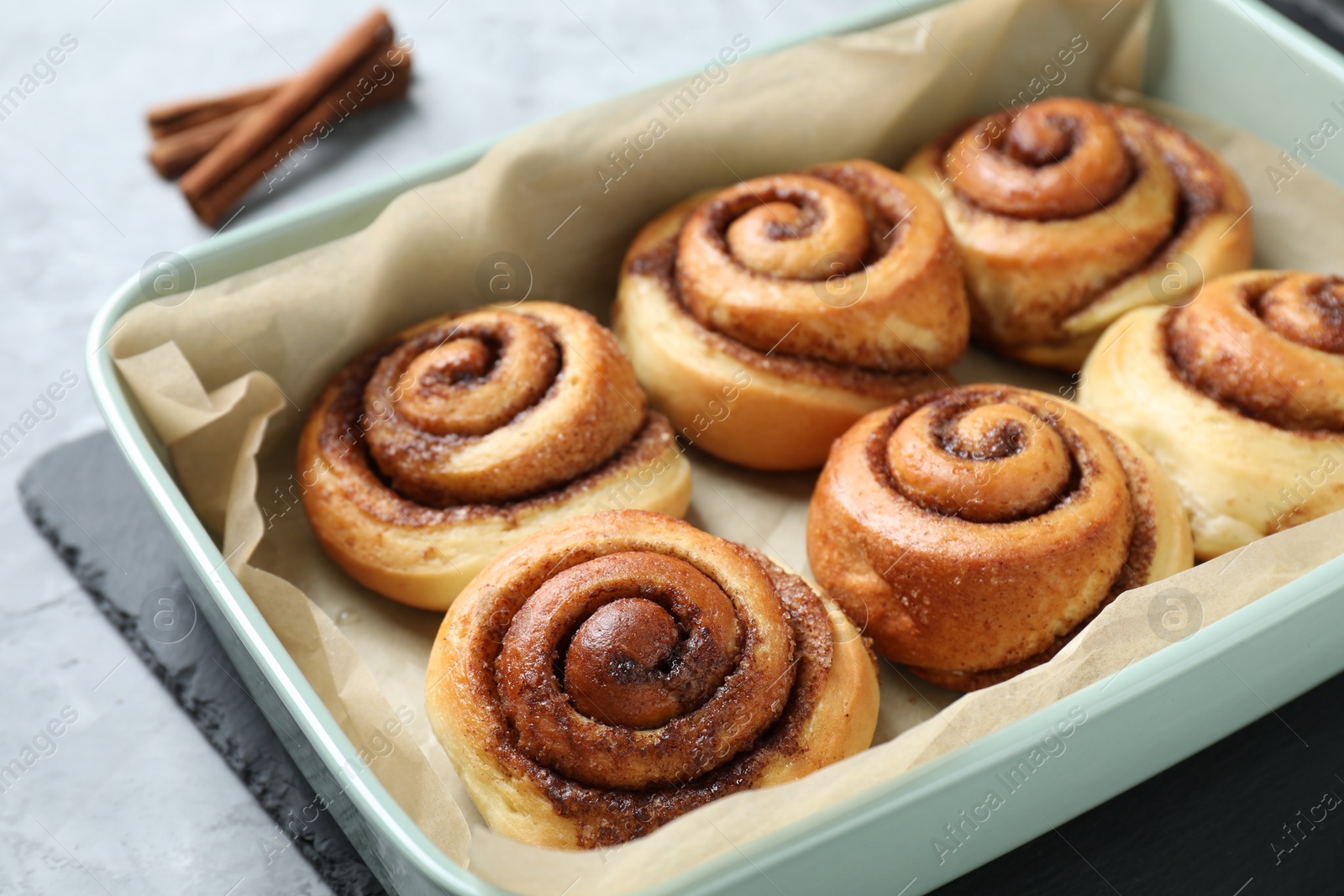 Photo of Baking dish with tasty cinnamon rolls on grey table, closeup