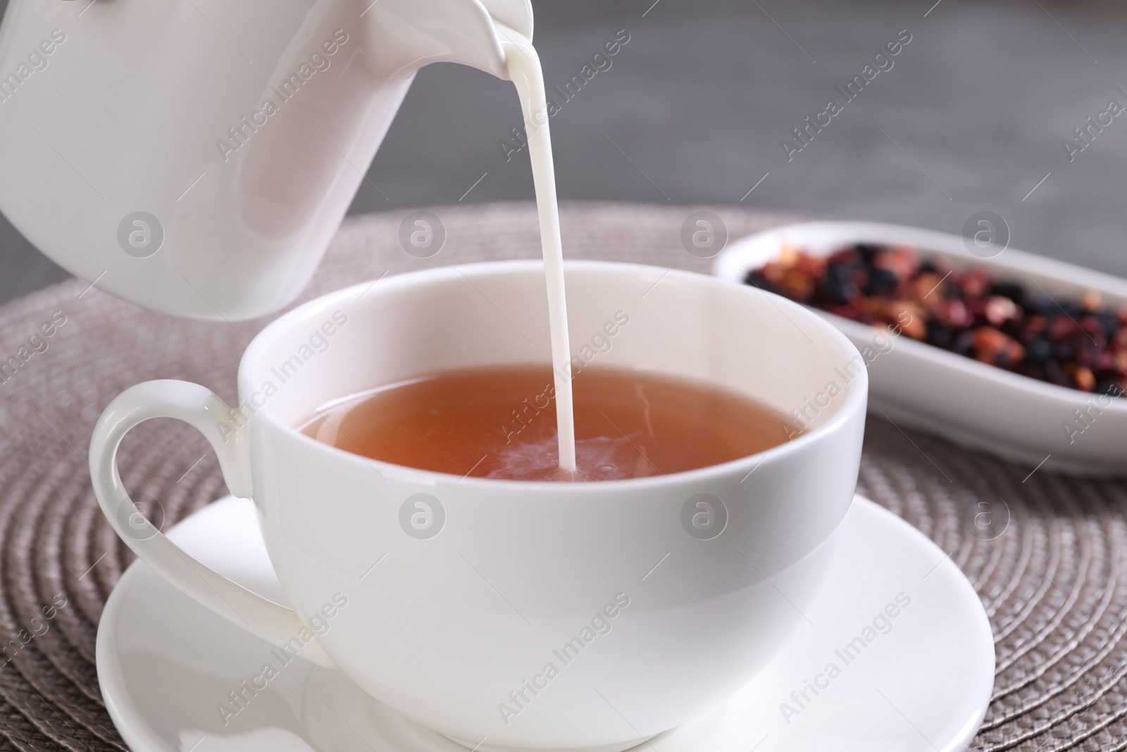 Photo of Pouring milk into cup with aromatic tea at table, closeup