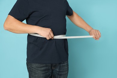 Photo of Man measuring waist with tape on light blue background, closeup