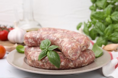 Photo of Raw homemade sausages and basil leaves on white table, closeup