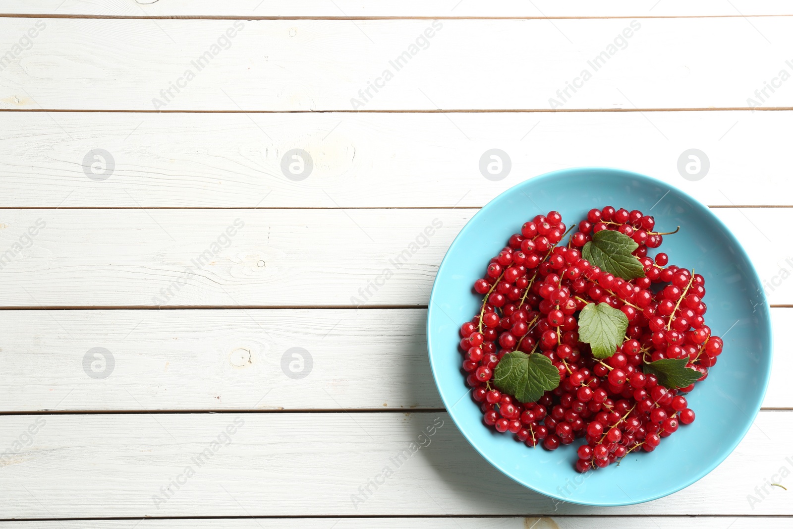 Photo of Delicious red currants and leaves on white wooden table, top view. Space for text