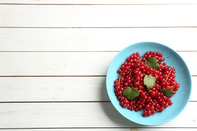 Photo of Delicious red currants and leaves on white wooden table, top view. Space for text