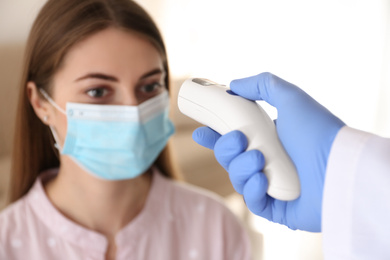 Doctor measuring patient's temperature with non contact infrared thermometer at home, closeup