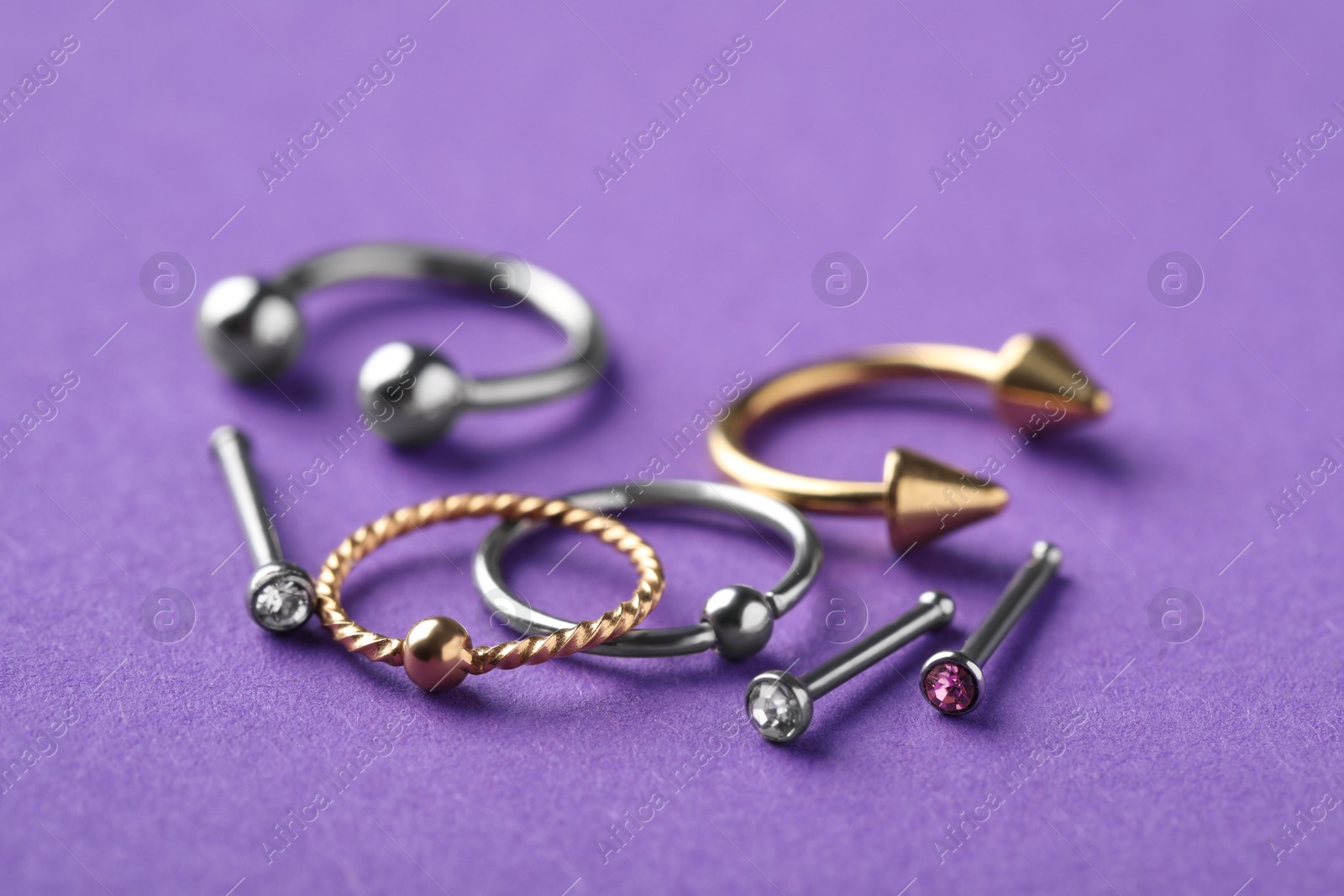 Photo of Stylish piercing jewelry on violet background, closeup