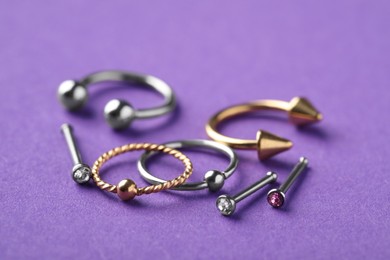 Photo of Stylish piercing jewelry on violet background, closeup