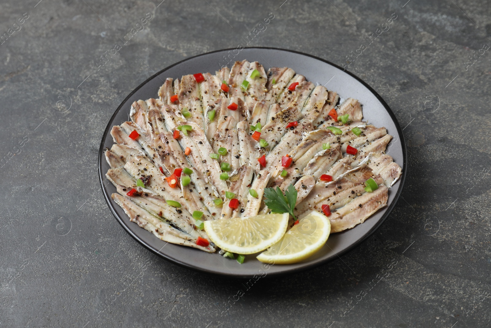 Photo of Tasty pickled anchovies with spices on grey textured table