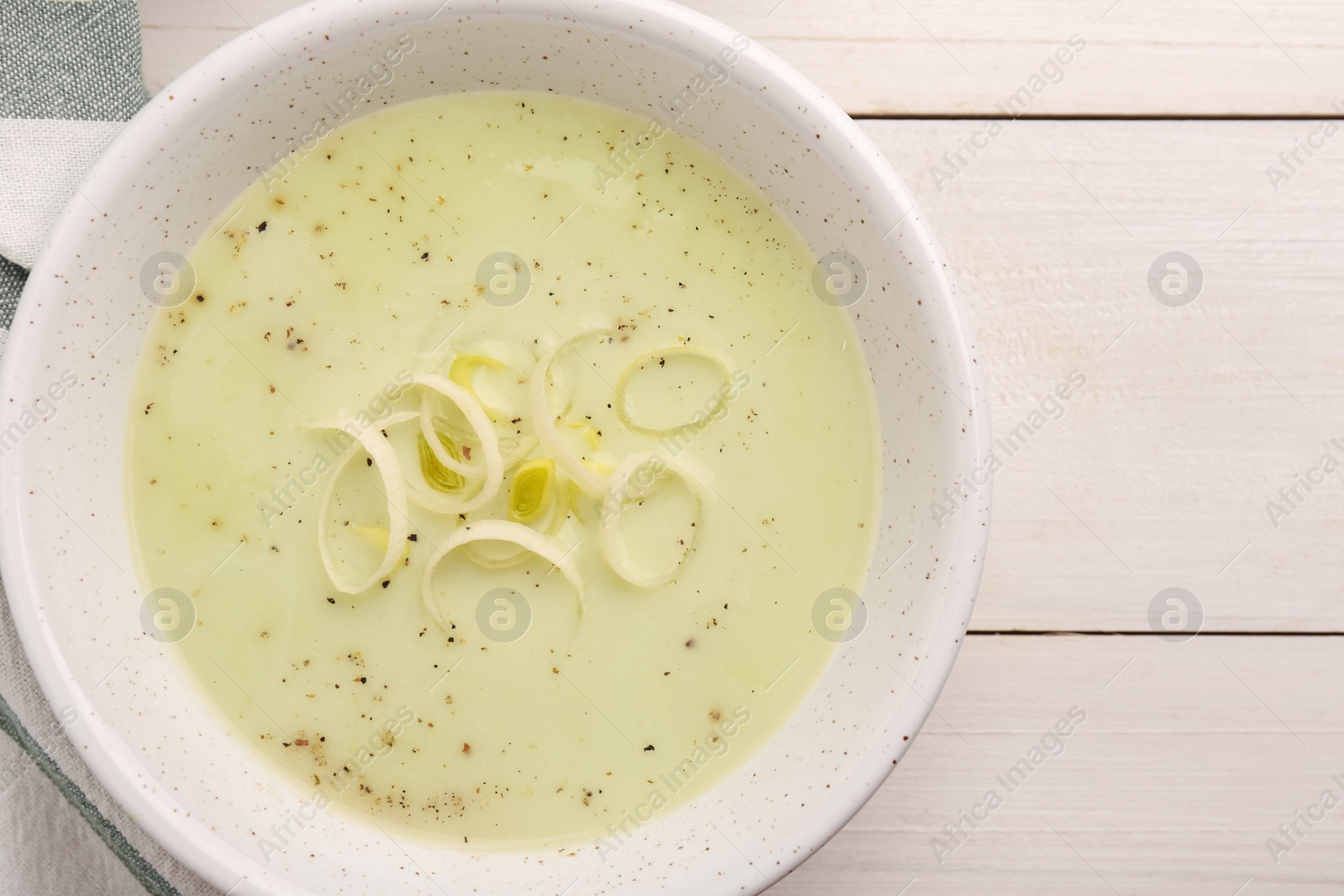 Photo of Bowl of tasty leek soup on white wooden table, top view. Space for text