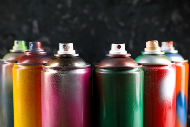 Photo of Used cans of spray paint on black marble background, closeup