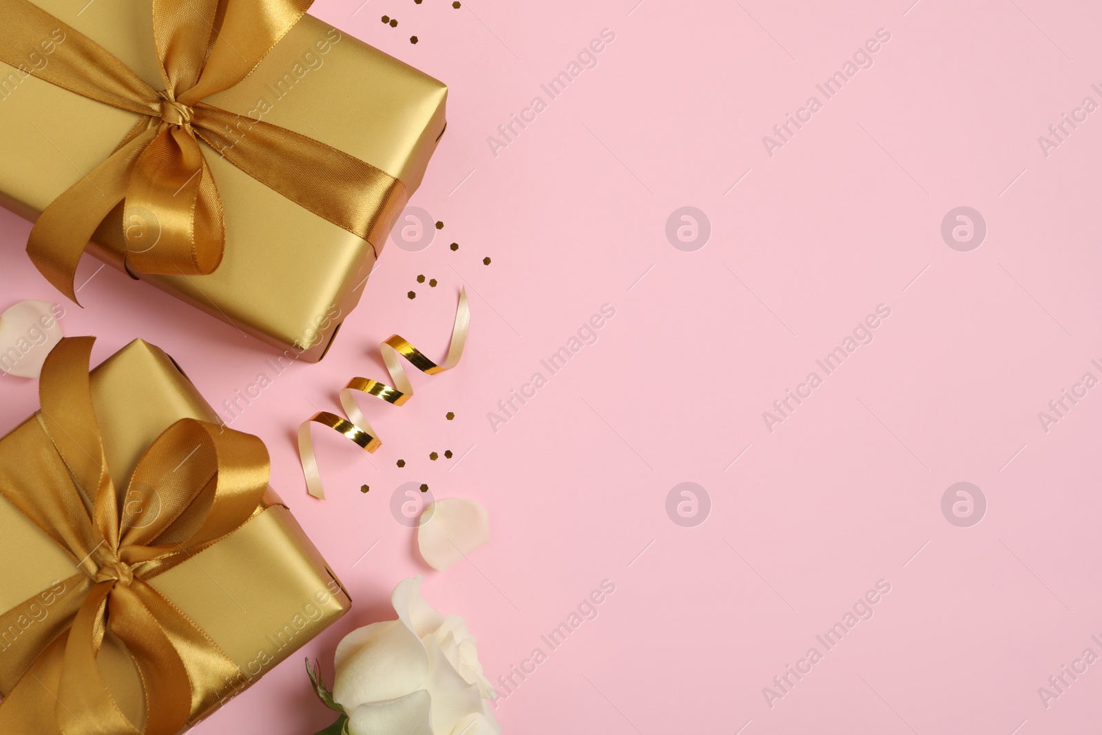 Photo of Two golden gift boxes, white rose, confetti and streamer on pink background, flat lay. Space for text