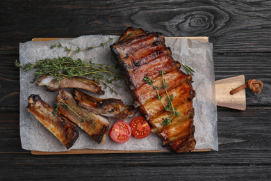 Tasty grilled ribs on black wooden table, flat lay