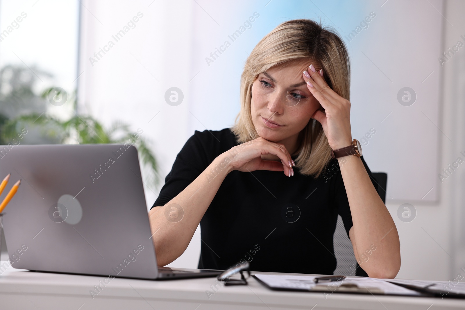Photo of Overwhelmed woman sitting at table with laptop and documents in office