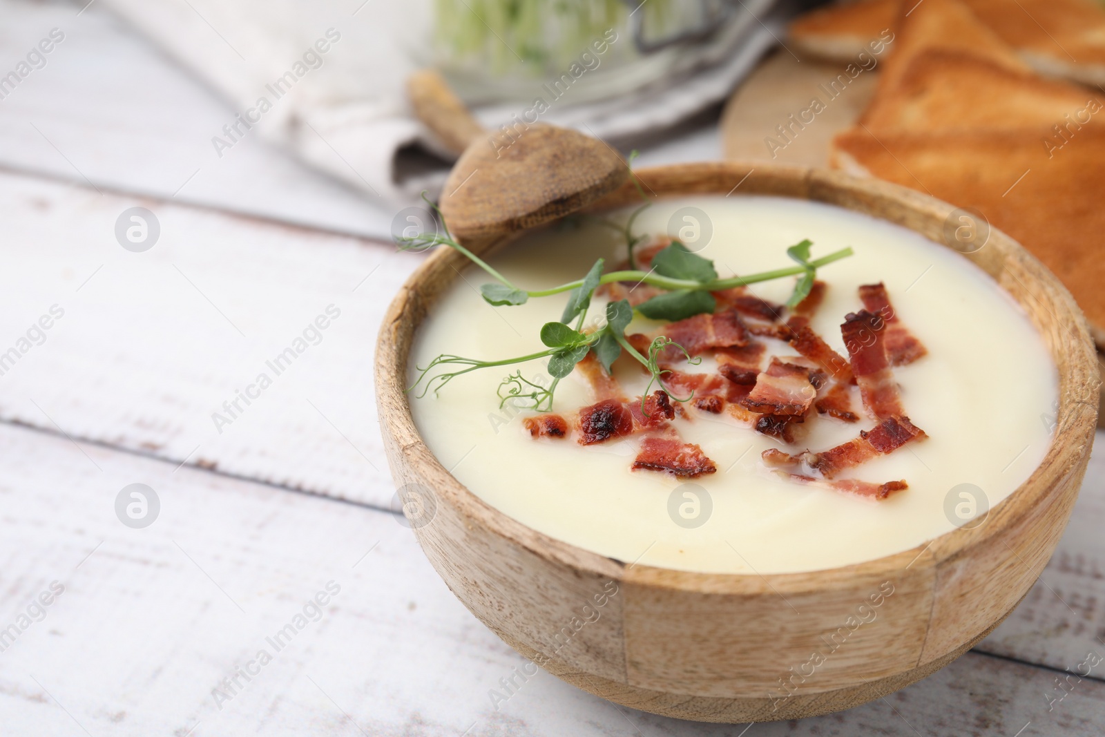 Photo of Delicious potato soup with bacon and microgreens in bowl served on wooden table, closeup. Space for text