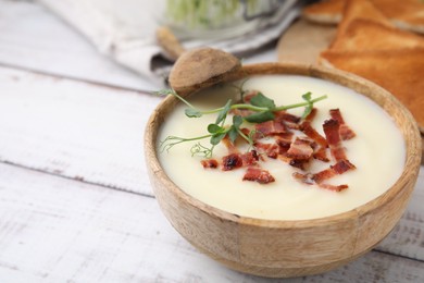 Delicious potato soup with bacon and microgreens in bowl served on wooden table, closeup. Space for text