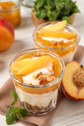 Photo of Tasty peach yogurt with granola, pieces of fruit and jam on white wooden table