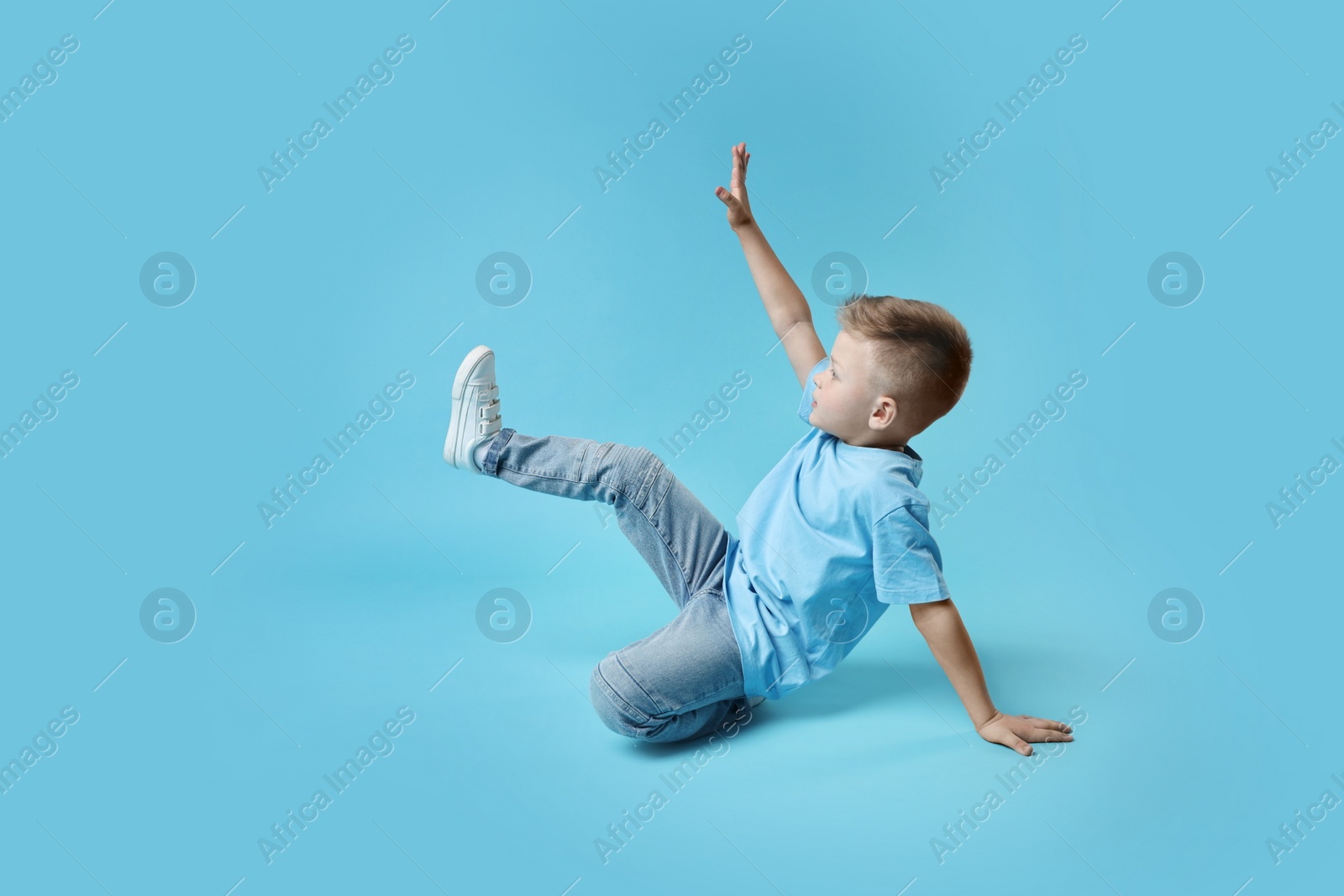 Photo of Happy little boy dancing on light blue background. Space for text