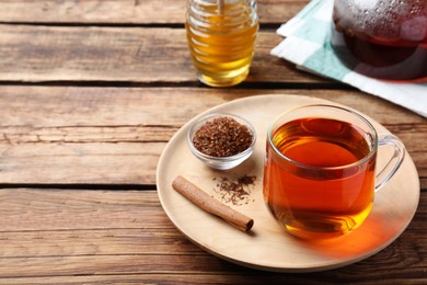 Photo of Freshly brewed rooibos tea, dry leaves and cinnamon stick on wooden table. Space for text