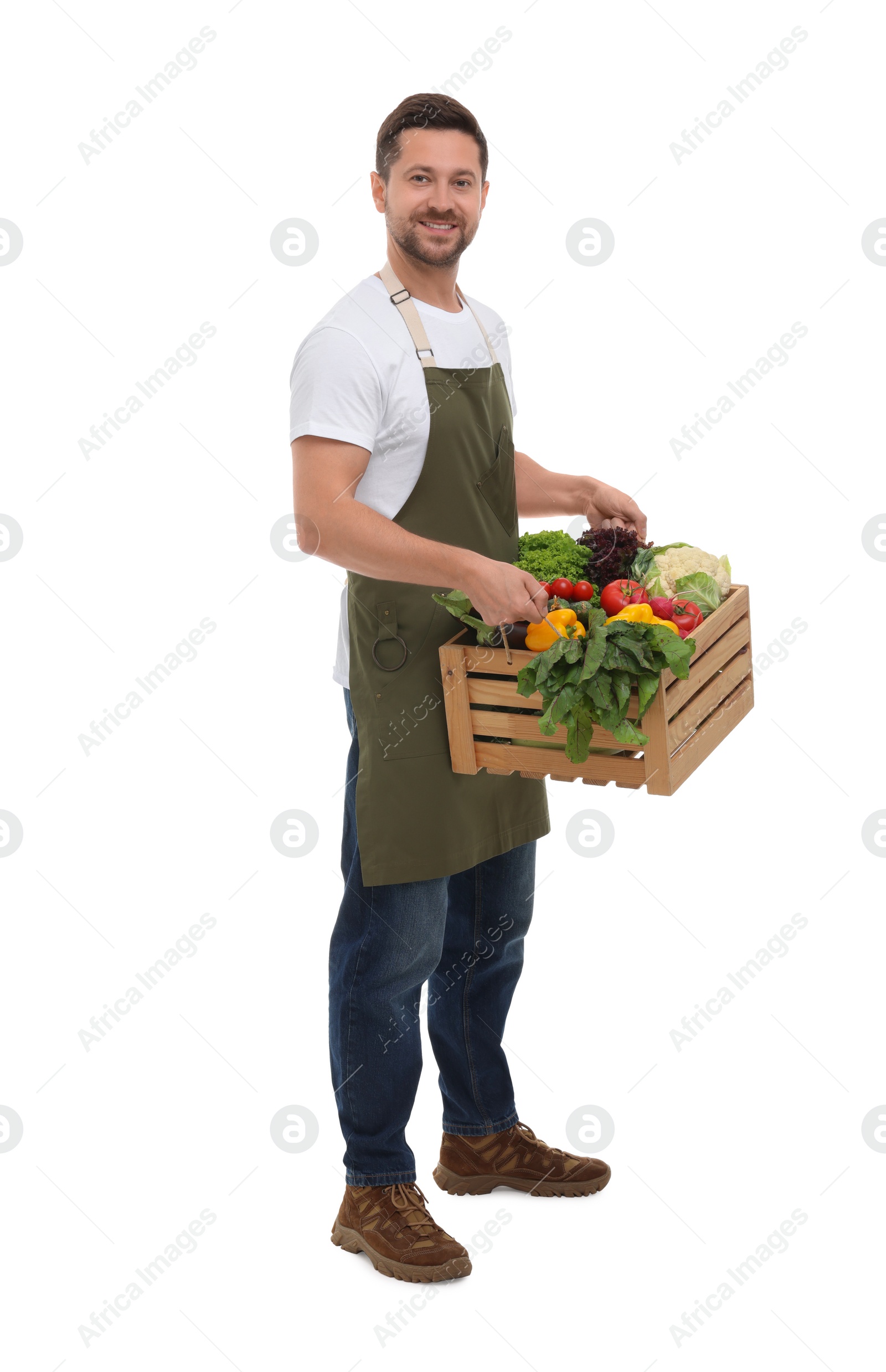 Photo of Harvesting season. Happy farmer holding wooden crate with vegetables on white background