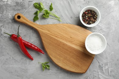 Photo of Cutting board, salt, spices, chili peppers and parsley on grey textured table, flat lay. Space for text