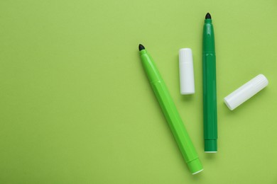 Photo of Bright markers and caps on light green background, flat lay. Space for text