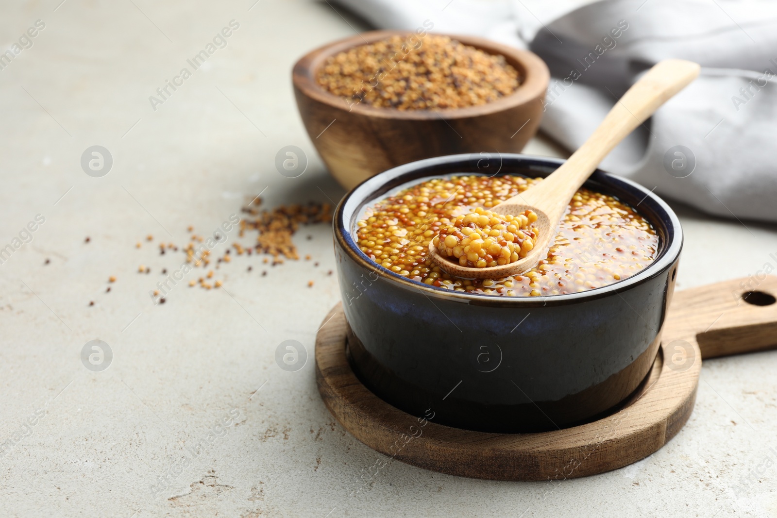 Photo of Whole grain mustard in bowl and spoon on light table. Space for text