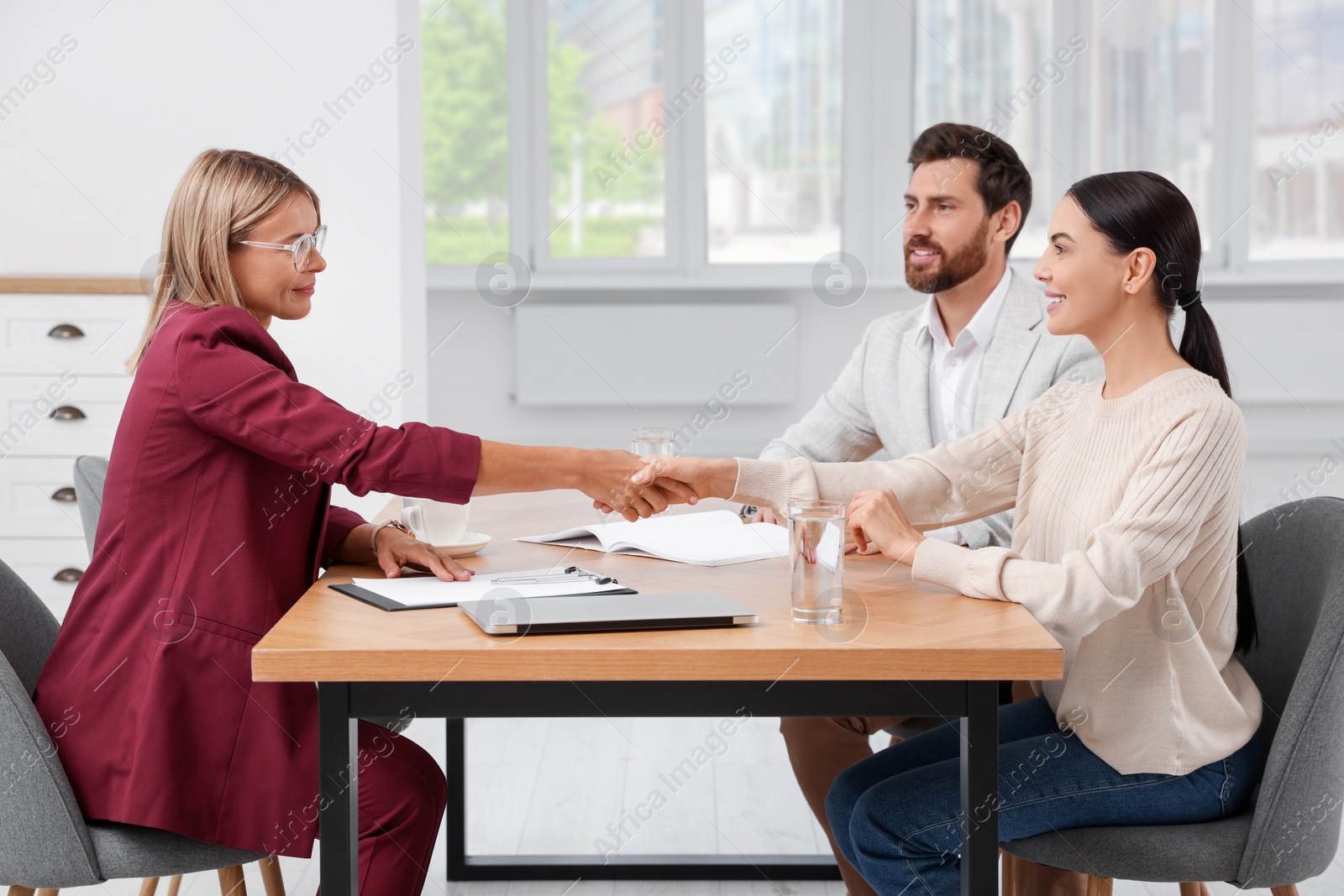 Photo of Real estate agent shaking hands with client at table in new apartment