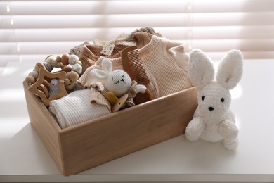 Photo of Wooden crate with children's clothes, toys and pacifier on white table near window