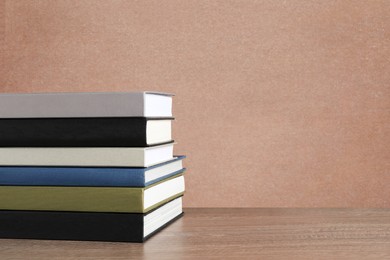 Many stacked hardcover books on wooden table against beige textured background, space for text