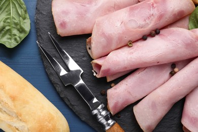 Rolled slices of delicious ham and baguette served on blue wooden table, flat lay