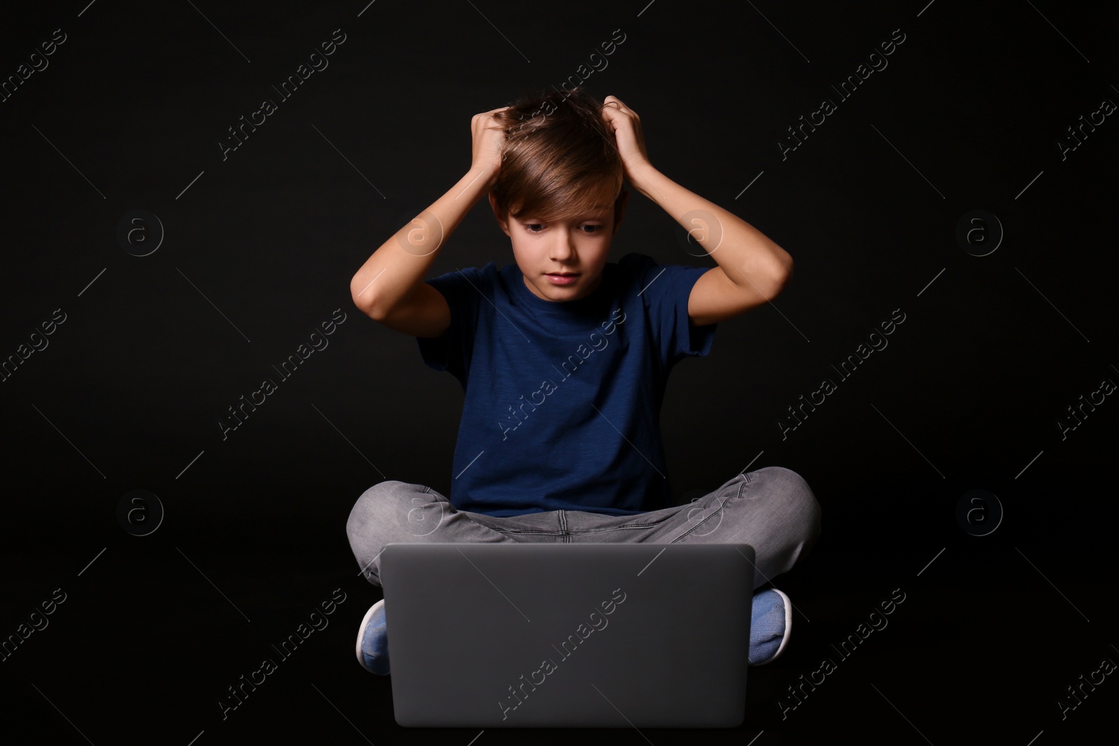 Photo of Shocked child with laptop on black background. Danger of internet