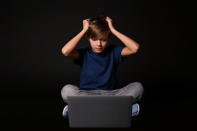 Shocked child with laptop on black background. Danger of internet