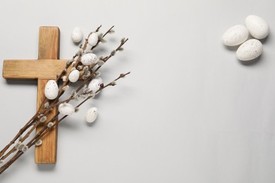 Wooden cross, painted Easter eggs and willow branches on light grey background, flat lay. Space for text