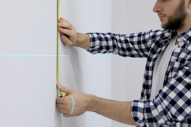 Man using cross line laser level and tape for accurate measurement on light wall, closeup